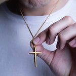 A close-up of a person wearing a white t-shirt and holding a gold cross pendant on a gold chain necklace.