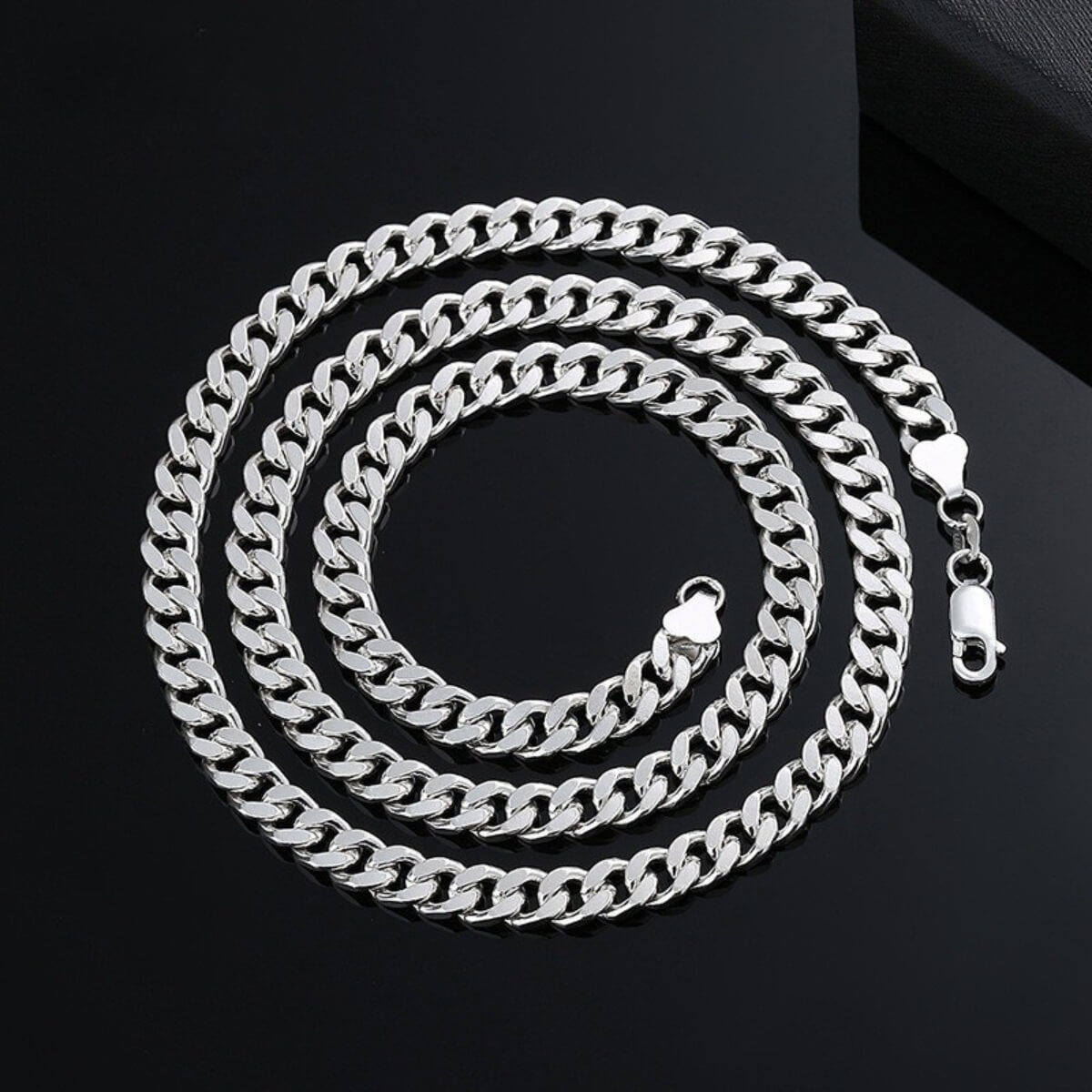 Sterling silver Cuban link chain coiled on black background, clasp detail visible